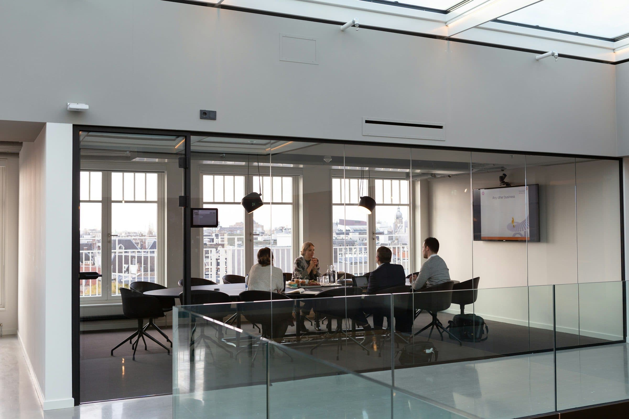 A small group meeting around a table inside a glass-walled conference room in a bright modern office