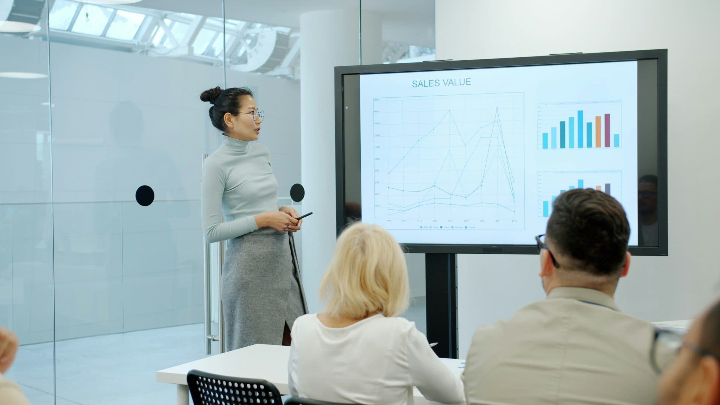 Colleague presenting data charts on a large screen to a small team in a meeting room